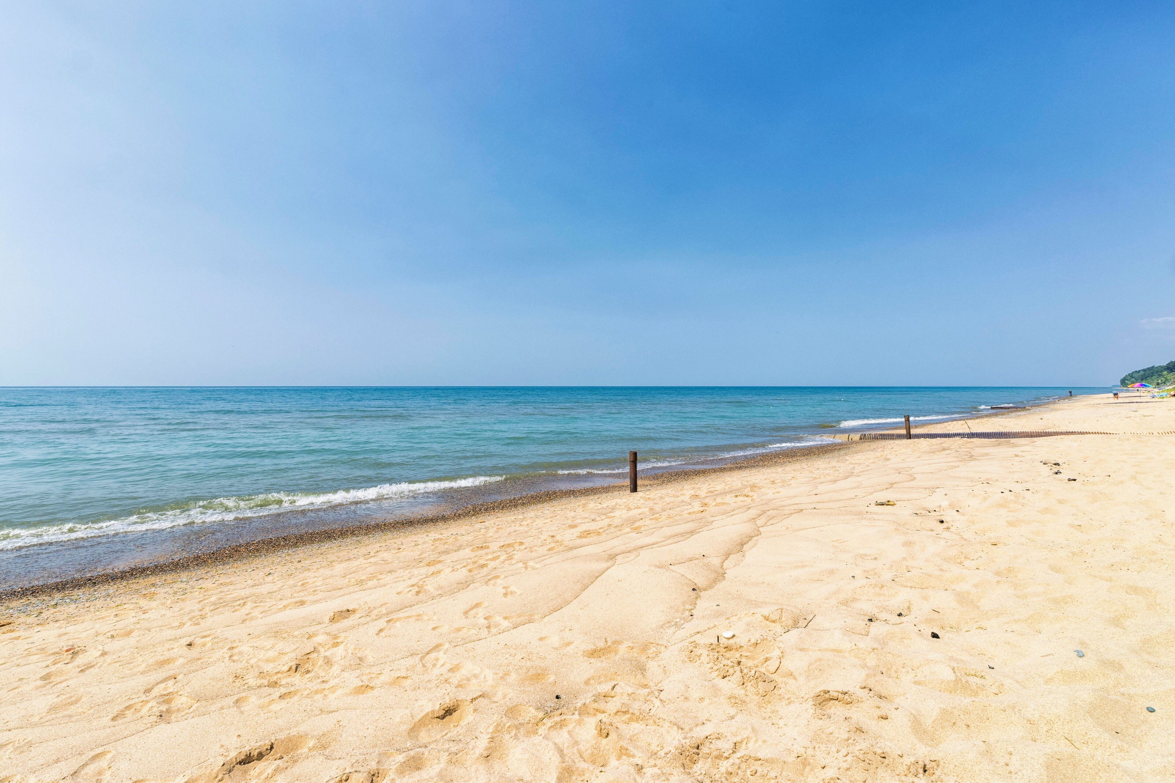 A wide sandy beach with gentle waves, a clear sky, and a distant shoreline.
