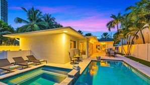 A swimming pool area with lounge chairs and a small building, surrounded by palm trees. - Steps to Beach / Heated Pool / Kiwi Key / Residences (Fort Lauderdale)