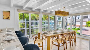 A dining area with a long table set for six, surrounded by wooden chairs, large windows with a view of greenery, and a ceiling with exposed beams. - Steps to Beach / Heated Pool / Kiwi Key / Residences (Fort Lauderdale)