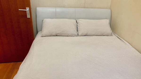 A bed with a striped bedspread and two pillows, a wooden door, and a light-colored wall. - Beijing CBD - Studio Apartment Queenbeds (Beijing)