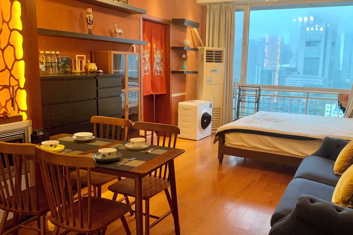Ein Hotelzimmer mit Bett, Esstisch mit Stühlen, Küchenzeile und Blick auf die Stadt durch das Fenster.