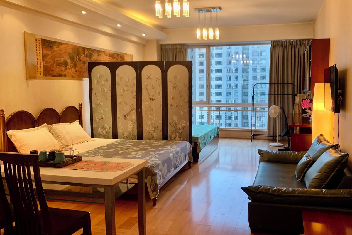 Ein Hotelzimmer mit einem Bett, einer Couch, einem Esstisch und einem großen Fenster mit Blick auf Gebäude.