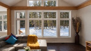 Un salon chaleureux avec une grande fenêtre donnant sur une forêt enneigée.