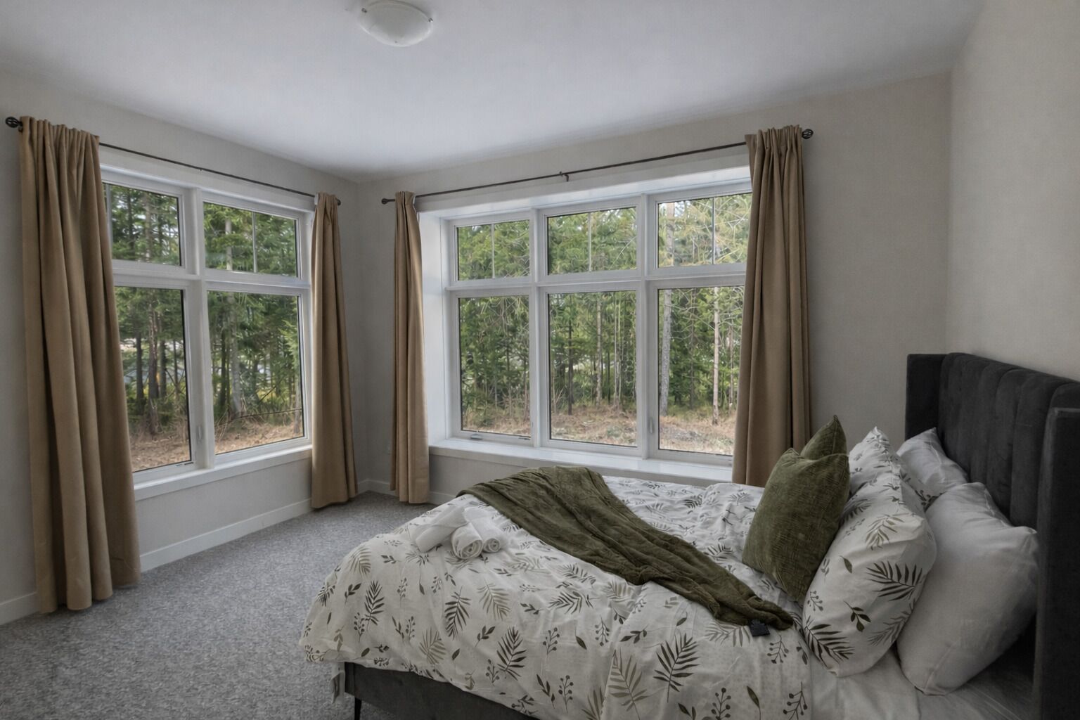 Un dormitorio con cama, dos ventanas y vista a árboles.
