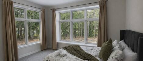 Un dormitorio con cama, dos ventanas y vista a árboles.