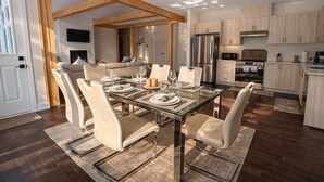 Une cuisine moderne avec des poutres en bois, des appareils en acier inoxydable et un coin repas comprenant une table en verre et des chaises rembourrées.
