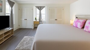 Une chambre d’hôtel avec un grand lit, un téléviseur posé sur un meuble, un bureau avec une chaise et deux portes.