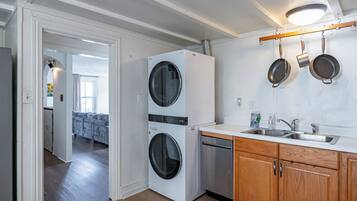 Een compacte keuken met een ingebouwde wasmachine en droger, houten kastjes en een hangende rek voor pannen.