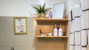 A bathroom with a toilet, a shower, a sink, and a shelf with toiletries. - Orchids @ Shore Residences 1BR Pool Access (Pasay City)