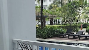 A balcony with a view of a swimming pool, a trash bin, and a chair. - Orchids @ Shore Residences 1BR Pool Access (Pasay City)