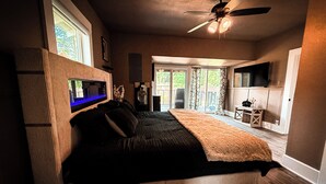 Un dormitorio con cama, ventilador de techo, televisión y vistas al exterior.