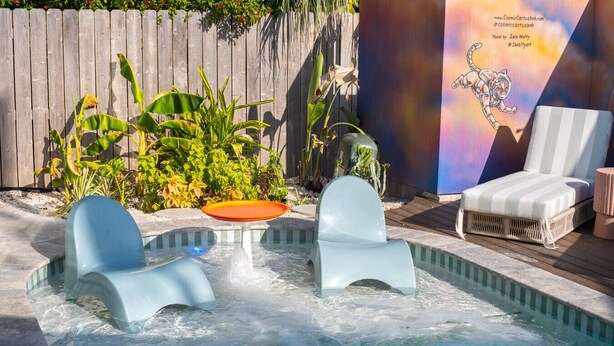 A hot tub area with two chairs and a table, surrounded by plants and a mural. - Venus B | Luxury 3BR + Pool & Steps to Beach (South Padre Island)