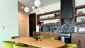 A modern kitchen with a wooden table and green chairs, a microwave, and a stove. - Venus D | Futuristic 2BR + Pool & Near Beach (South Padre Island)