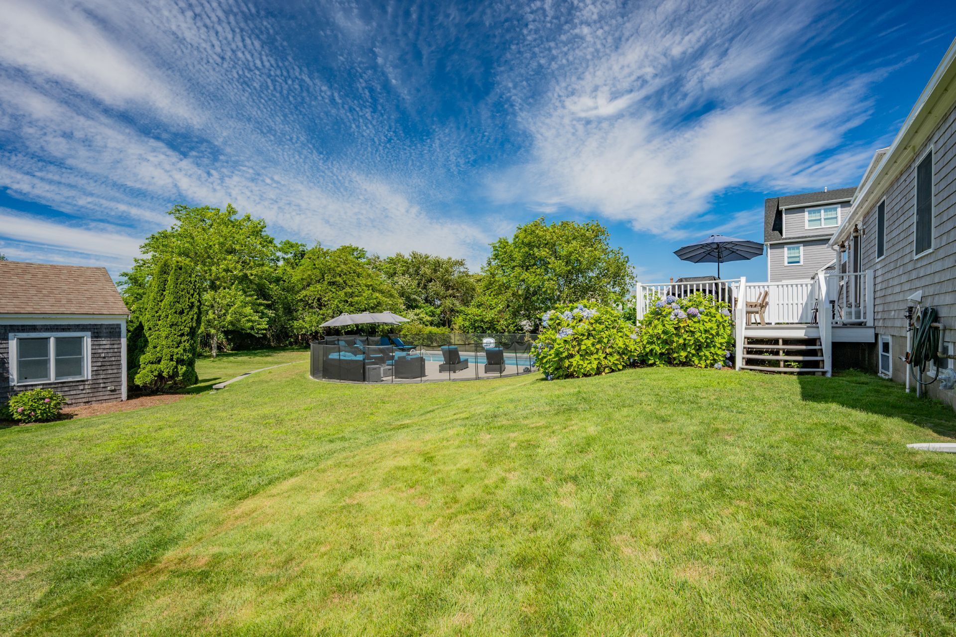 A backyard with a pool, a covered seating area, and a deck.