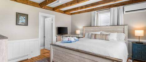 A bedroom with a wooden bed, white walls, a wooden ceiling, a television, and a window with curtains.
