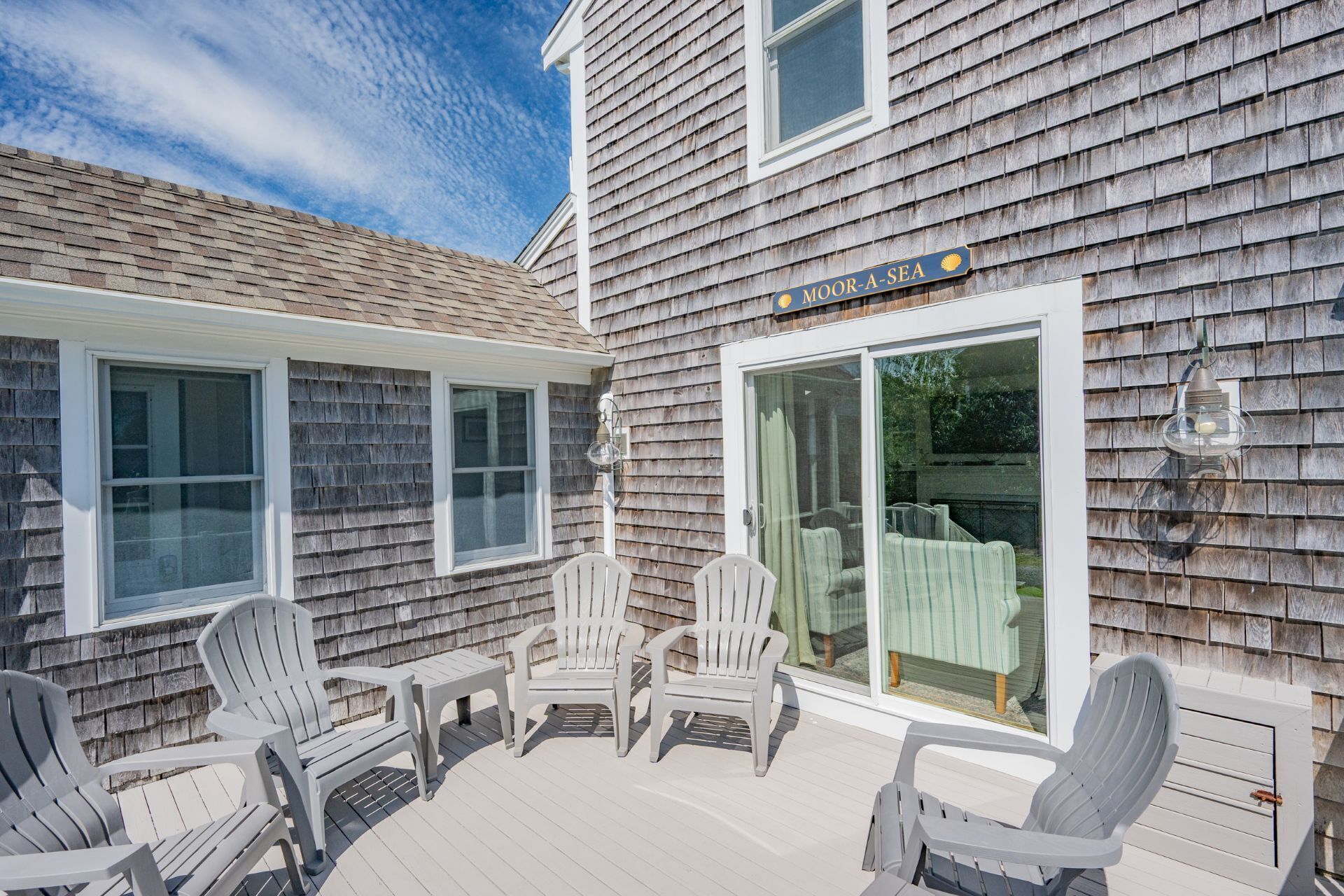 A wooden house with a deck featuring white plastic chairs and a table.