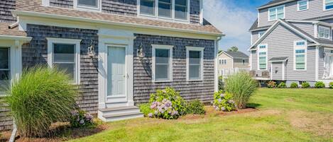 A two-story house with a front porch, a small garden with hydrangeas, and a clear blue sky.