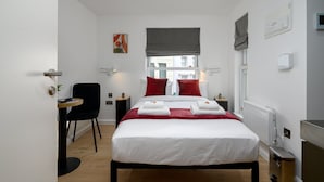 Ett modernt hotellrum med en stor säng, ett skrivbord, en stol och ett fönster med utsikt över byggnader.