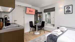 Een moderne hotelkamer met een bed, een bureau met twee stoelen, een kleine tafel met een plant, een televisie en een raam met uitzicht.