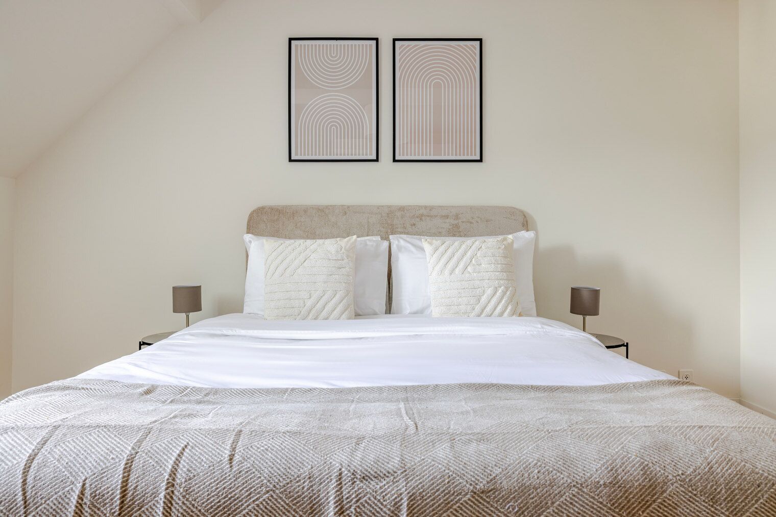 A neatly made bed with a textured blanket, two pillows, and a headboard. There are two wall-mounted picture frames above the bed.