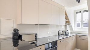 Une cuisine moderne avec un plan de travail noir, des appareils en acier inoxydable et des meubles de couleur claire.