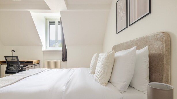 Une chambre à coucher avec un grand lit, un bureau avec une chaise, un radiateur et des œuvres d’art encadrées accrochées au mur.
