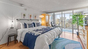 A modern bedroom with a large bed, a desk, and a view of the city through large windows. - Charming condo in lovely Honolulu with AC (Honolulu)