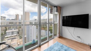 A modern room with large windows, a flat-screen TV, and a view of a cityscape. - Charming condo in lovely Honolulu with AC (Honolulu)