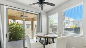 A dining area with a round table and four chairs, a ceiling fan, and a sliding glass door leading to an outdoor area. - Charming 2-bedroom townhome near ASU in Tempe  with AC, garage, and a pool! (Tempe)