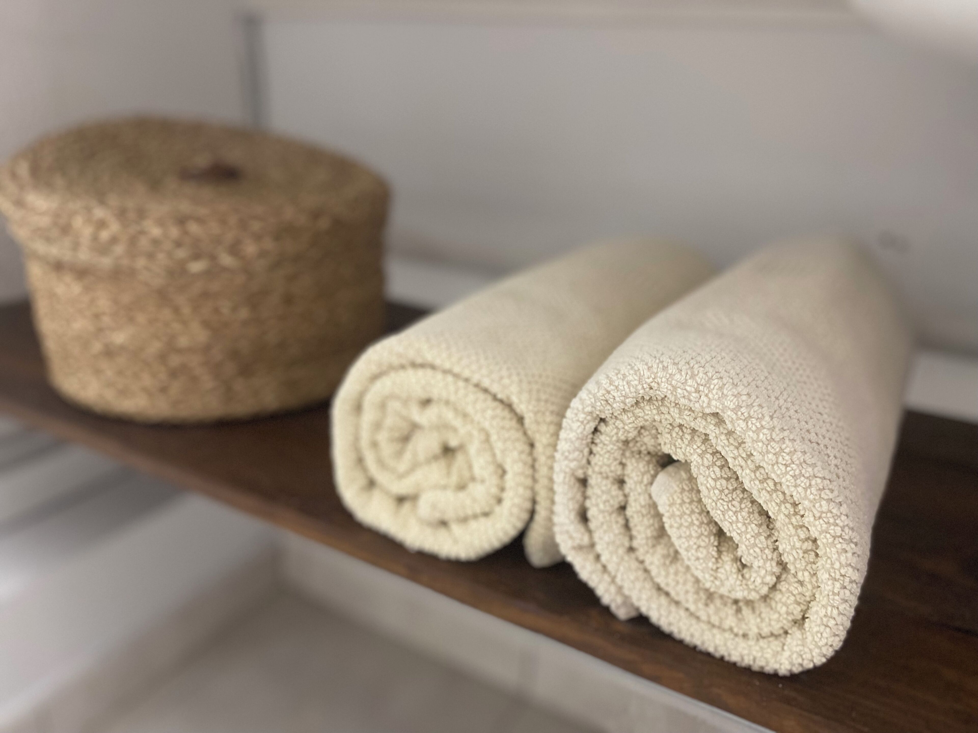 A shelf with a rolled beige towel and a round beige container.