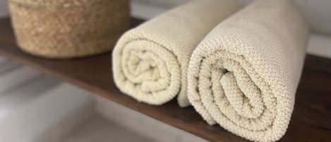 A shelf with a rolled beige towel and a round beige container.