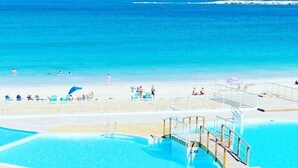A beach with a swimming pool, a lifeguard tower, and a distant lighthouse.