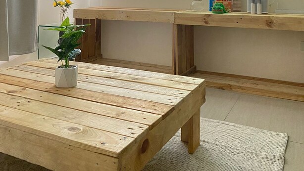 A room with a wooden table, a potted plant, a television displaying a coastal landscape, and a shelf with items. - Lavender @ Shore Residences 2BR (Pasay City)