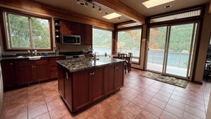 A spacious kitchen with a large island, wooden cabinets, and a view of a lake through large windows.