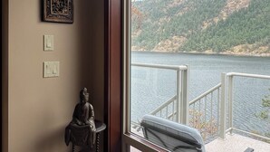 A room with a large window overlooking a lake and hills, a statue, and two wall-mounted light switches.
