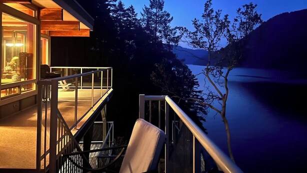 A modern building with a balcony overlooking a lake, surrounded by trees.