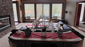 A spacious living room with a stone fireplace, large windows offering a view of a balcony, and a red rug with decorative items.