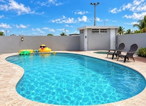 A swimming pool with a curved edge, a small structure with a door, and two chairs.