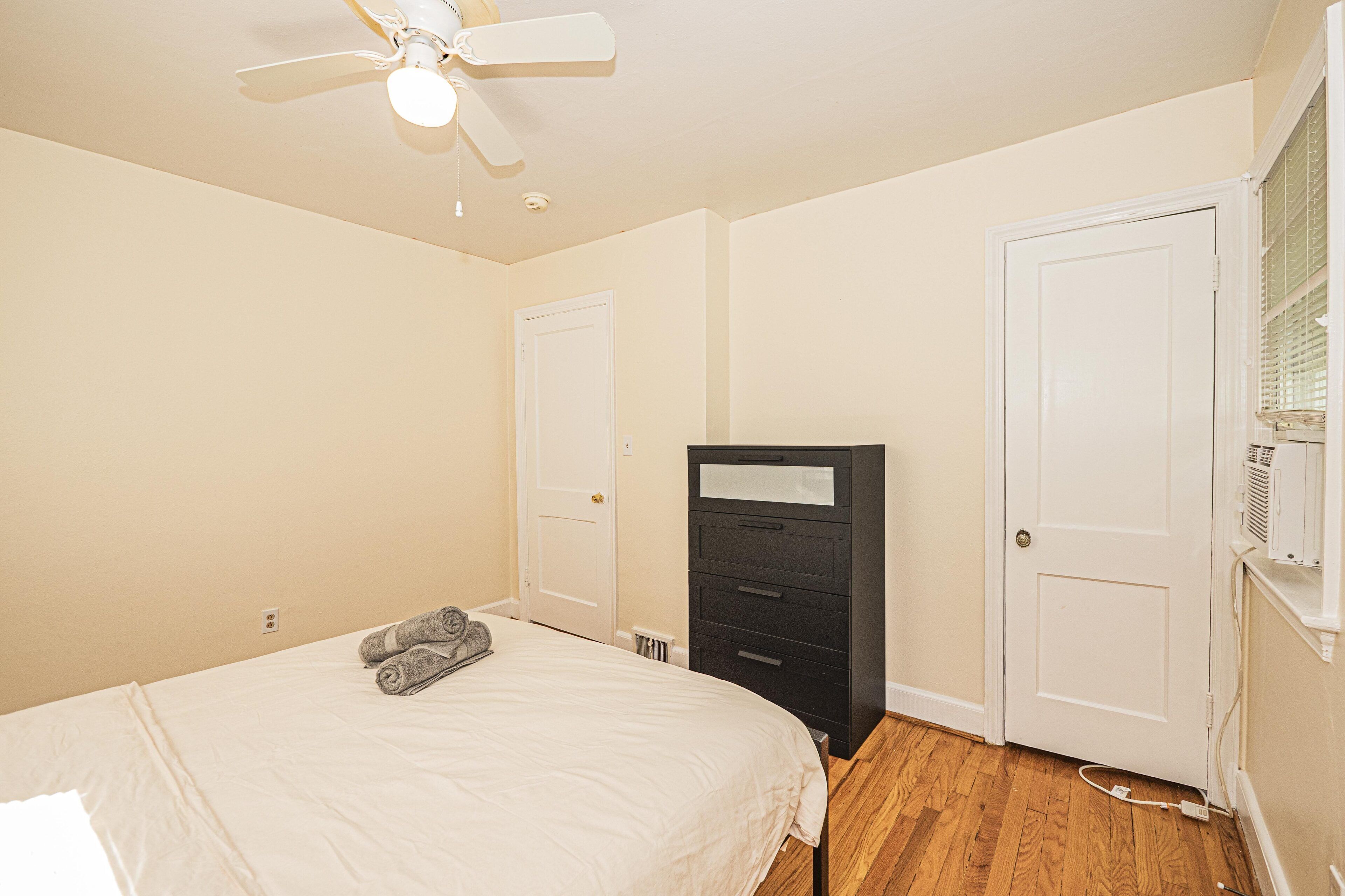 Une chambre à coucher avec un lit, un ventilateur de plafond, une commode et une porte.
