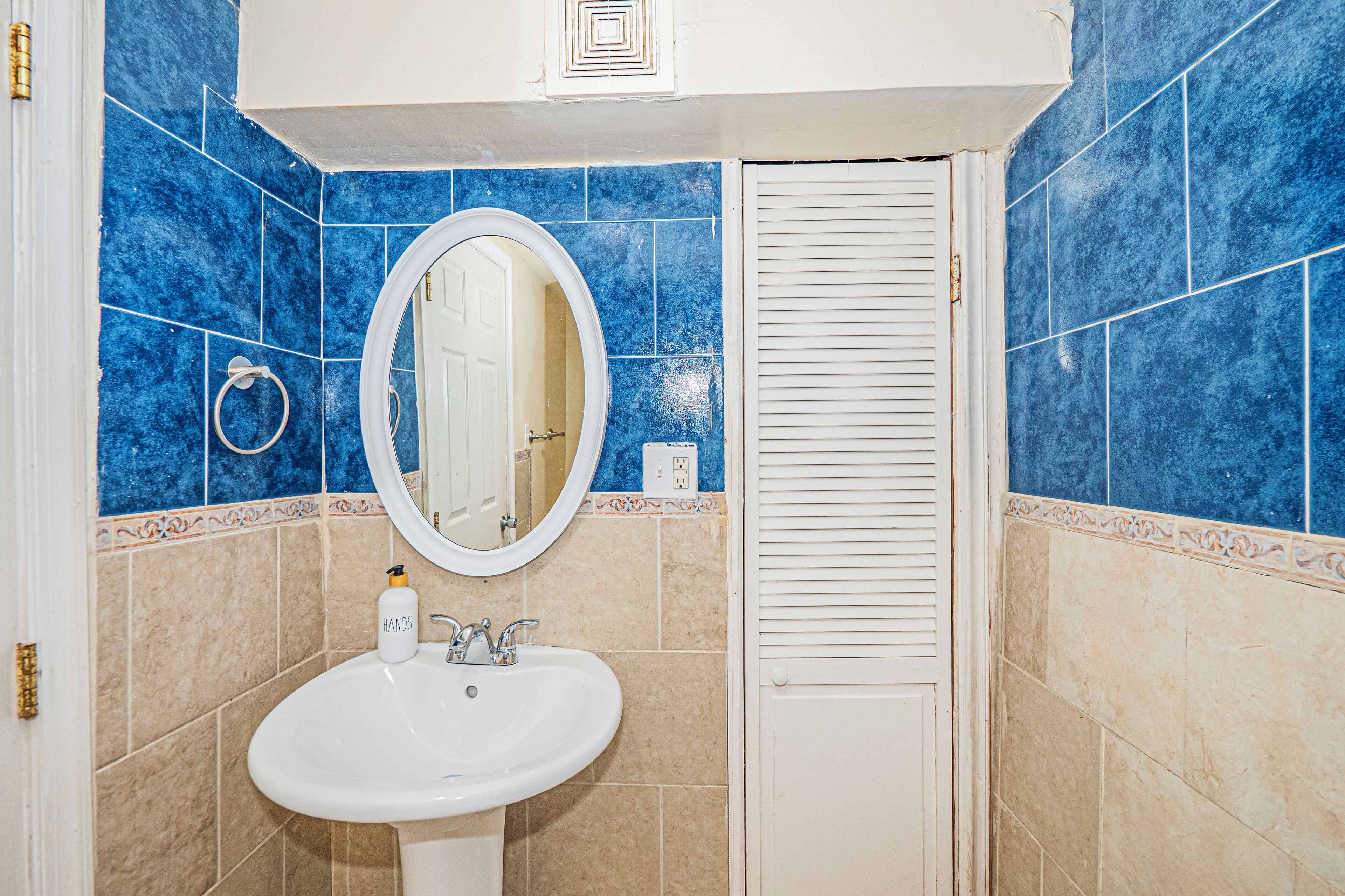 Une salle de bain avec un lavabo blanc, un miroir et des carreaux bleus.