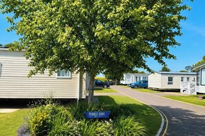Een stacaravanhaven met een laan vol bomen en een bord waarop 'PEBBLE COVE' staat.