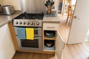 A compact kitchen with a gas stove, oven, and a small cabinet with a blue bowl. - Seaside Lodge Haven in St Osyth (St Osyth)