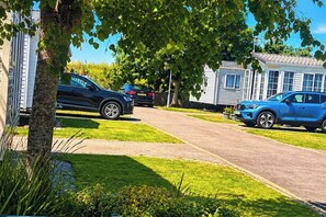Een woonstraat met twee stacaravans, een zwarte auto en een blauwe auto langs de kant.