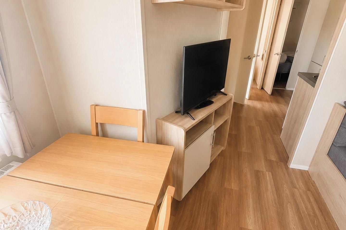 A compact room with a wooden table, a television on a stand, a chair, and a small cabinet.