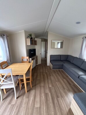 A compact living space with a dining table, chairs, a sofa, a television, and a mirror.