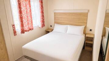 Habitación individual con una cama de madera, dos mesitas de noche y una ventana con cortinas rojas.