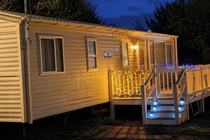 Een stacaravan met een veranda en een trap, omringd door bomen.