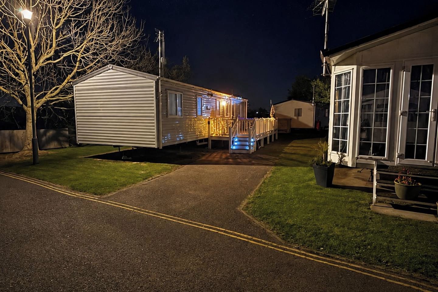 Un quartier résidentiel de nuit, avec une maison, une résidence mobile et un chemin bien éclairé.