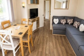 Een moderne woonkamer met een grijze bank, een houten eettafel en een televisie op een standaard.