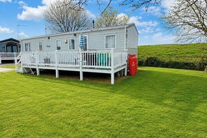 En campingvogn med en indhegnet terrasse, skorsten og græsplæne.